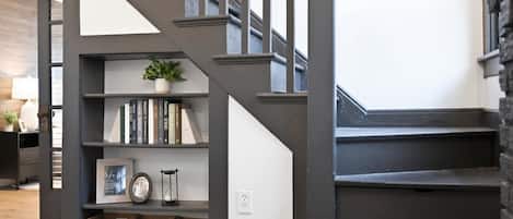 A staircase with a dark finish, a bookshelf with books and a potted plant, and wicker baskets at the bottom.