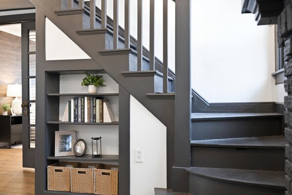 A staircase with a dark finish, a bookshelf with books and a potted plant, and wicker baskets at the bottom.