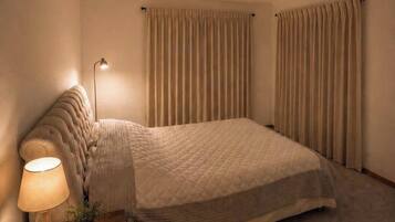 A bedroom with a bed, a nightstand with a lamp, a small plant, and a fur rug.