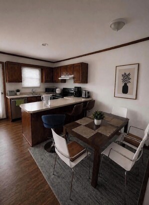 Een moderne keuken met houten kastjes, een centraal eiland en een eethoek met een tafel en stoelen.
