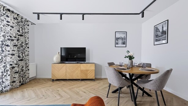 Una sala de estar moderna con comedor, un televisor sobre un mueble de madera y dos cuadros en la pared.