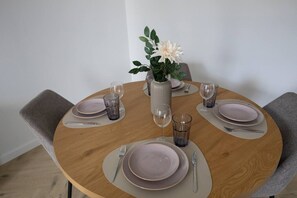 A round dining table with a vase of flowers, plates, cutlery, and glasses. - Warsaw Bemowo Apt – Underground Parking & Balcony (Warszawa)