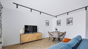 Una sala de estar moderna con un televisor sobre un mueble de madera, una mesa de comedor con sillas y un sofá azul.