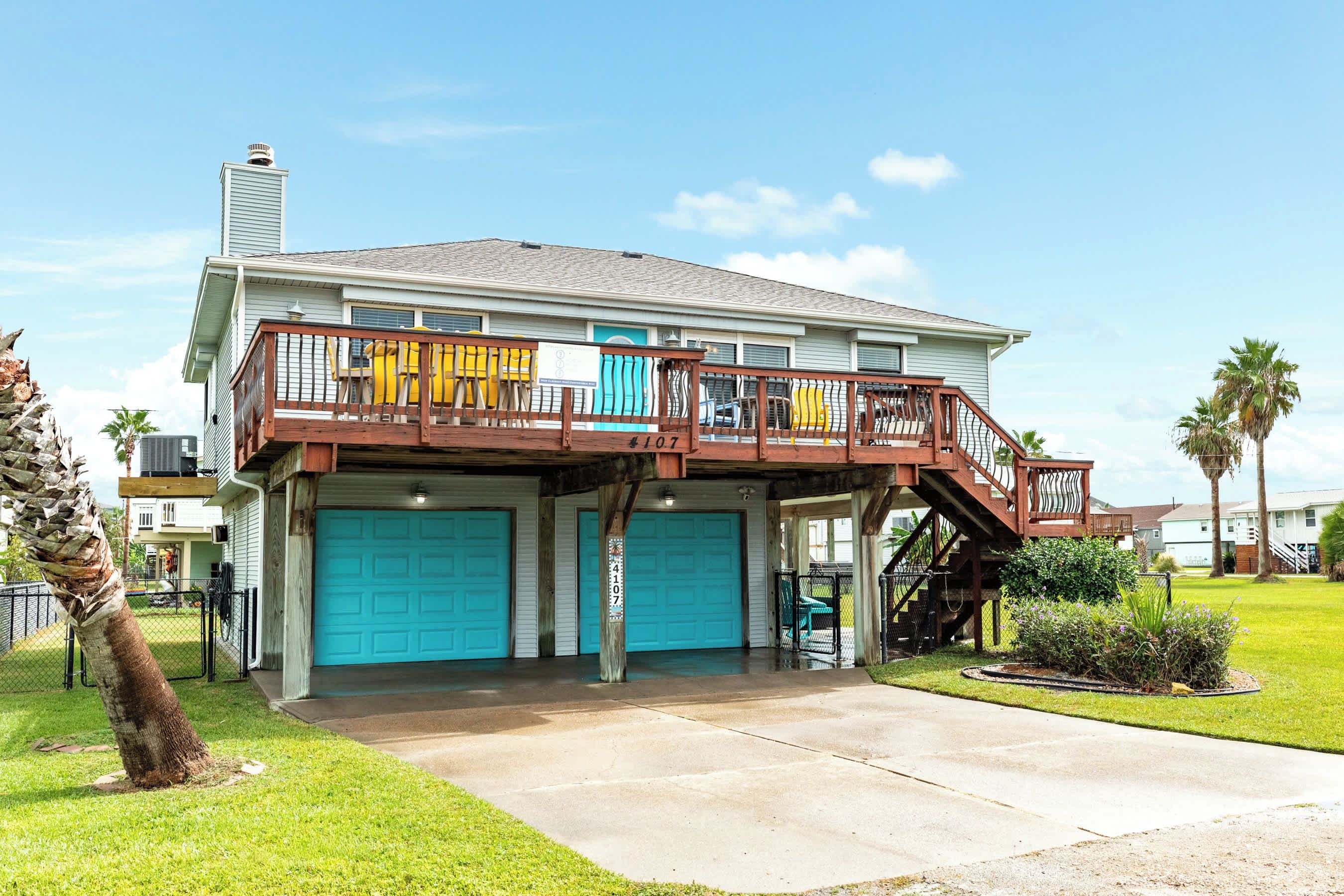 Ein zweigeschossiges Haus mit überdachter Veranda, einer Garage mit blauen Türen und einem kleinen Außenbereich mit Pflanzen.