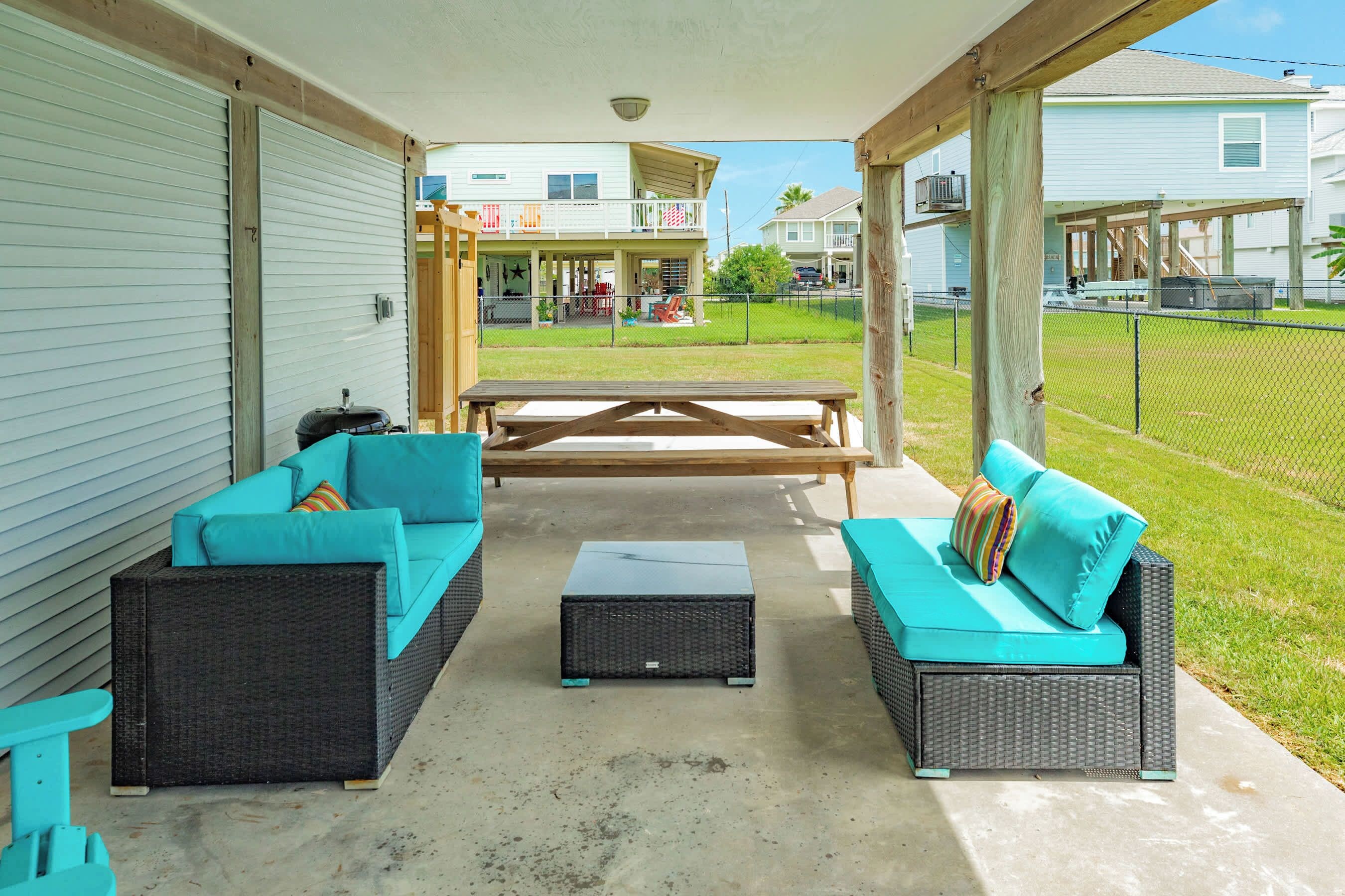 A covered patio area with outdoor furniture, a picnic table, and a view of a residential neighborhood.
