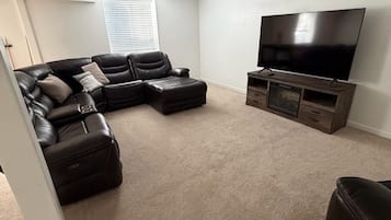A living room with a sectional sofa, ottoman, and a flat-screen TV on a wooden stand.