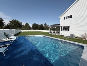 Una piscina con un deck cubierto de alfombra azul y sillas de descanso blancas.