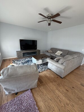 A living room with a grey sofa, a coffee table, a TV, and a ceiling fan. - Spacious Pool house in adorable Billings with AC. Big backyard + Covered Patio. (Billings)