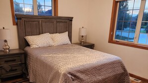 A bedroom with a bed, nightstands, a lamp, a window, and a view of the outdoors.
