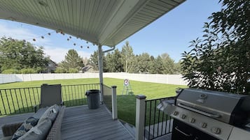 A covered patio with a grill, outdoor seating, and a lawn.