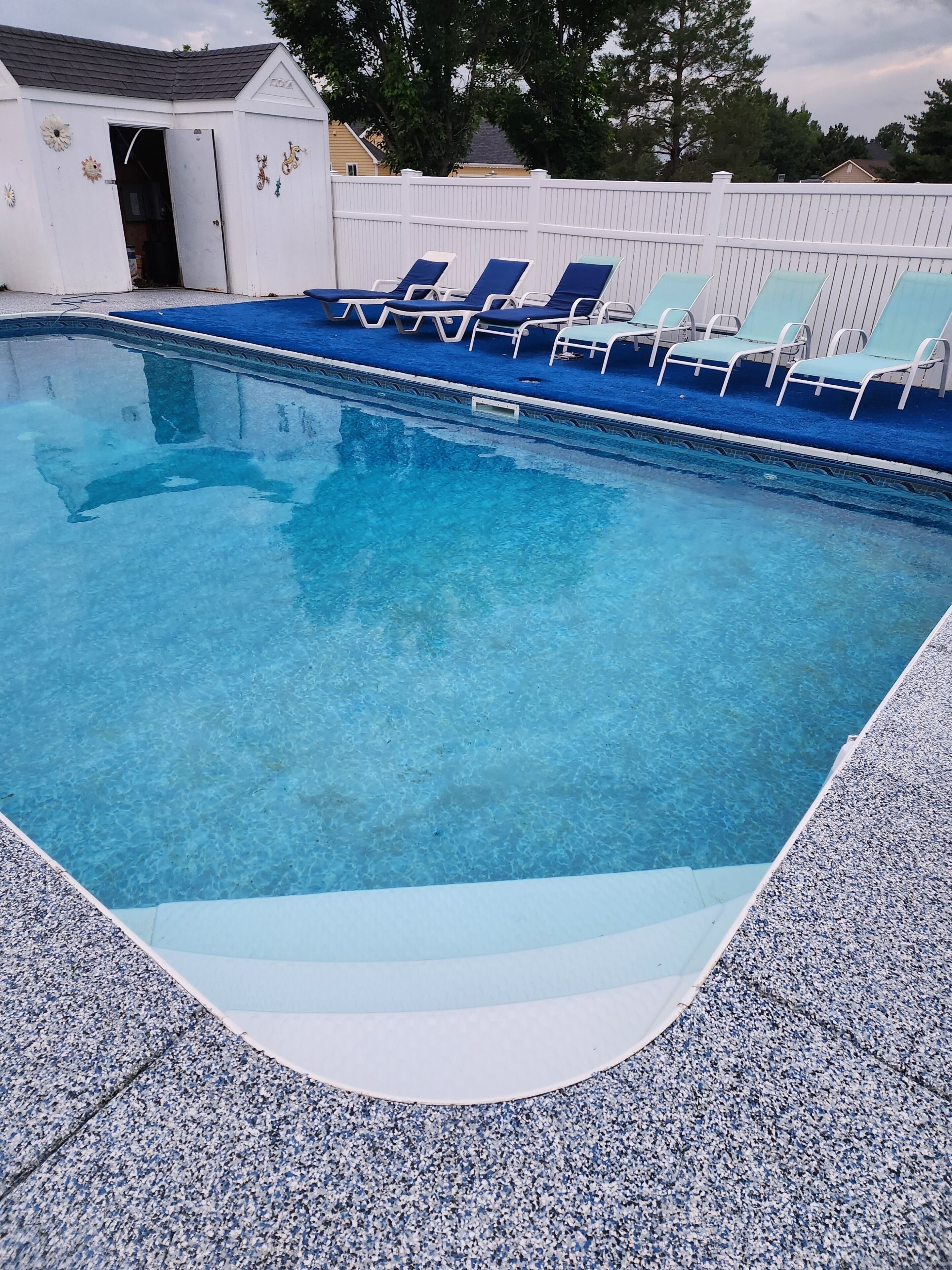 Piscina com água azul cristalina, rodeada por uma cerca branca e várias espreguiçadeiras.