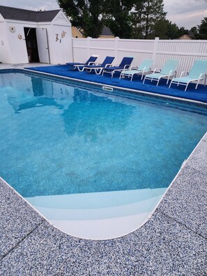 A swimming pool with clear blue water, surrounded by a white fence and several lounge chairs.
