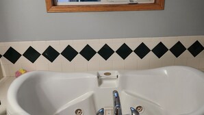 A bathroom with a white freestanding bathtub, a window above it, and a black and white patterned tile backsplash.