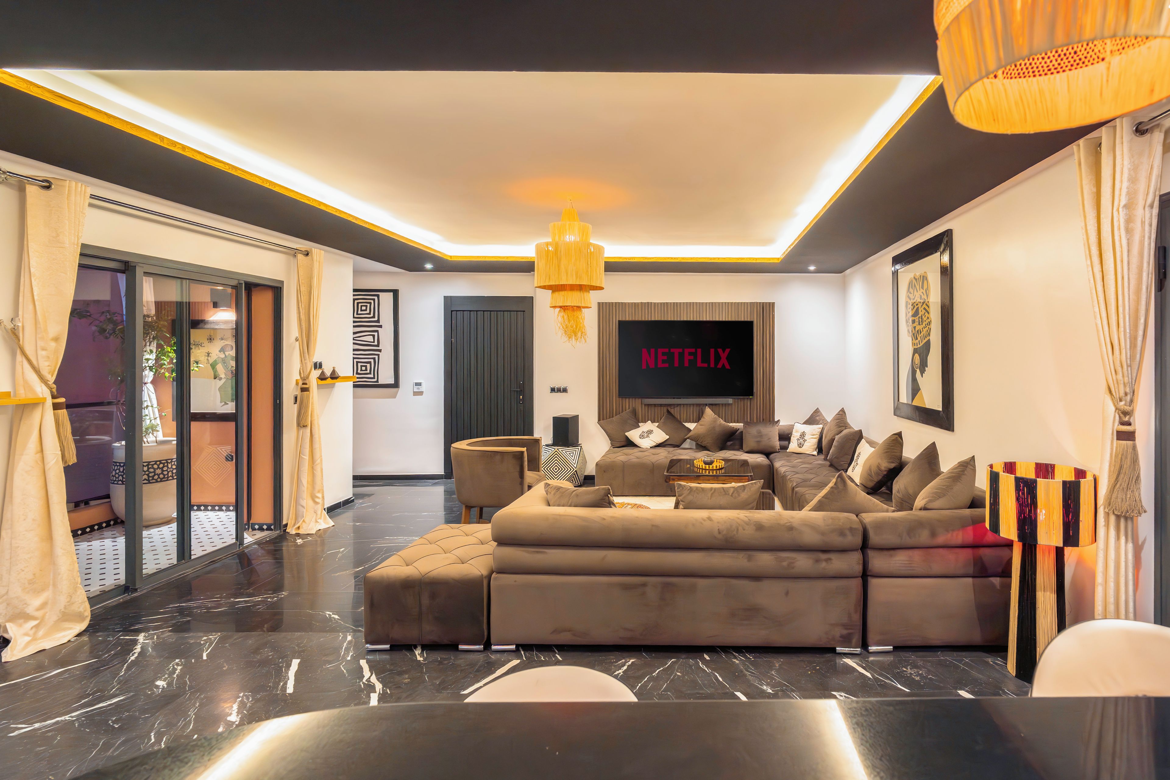 A modern living room with a sectional sofa, a flat-screen TV, and a chandelier.