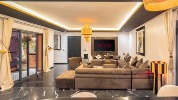 Een moderne woonkamer met een hoekbank, een flatscreen televisie en een kroonluchter.