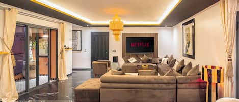 A modern living room with a sectional sofa, a flat-screen TV, and a chandelier.