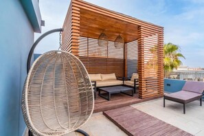 Un área de estar exterior moderna con una silla de mimbre, un sofá y una mesita.