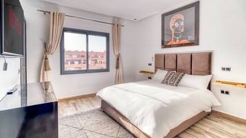 Une chambre moderne avec un grand lit, un téléviseur à écran plat, un plancher en bois et une vue sur les bâtiments à travers la fenêtre.