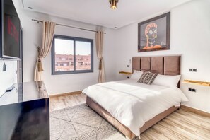 Un dormitorio moderno con una cama grande, un televisor de pantalla plana, piso de madera y vistas a edificios desde la ventana.