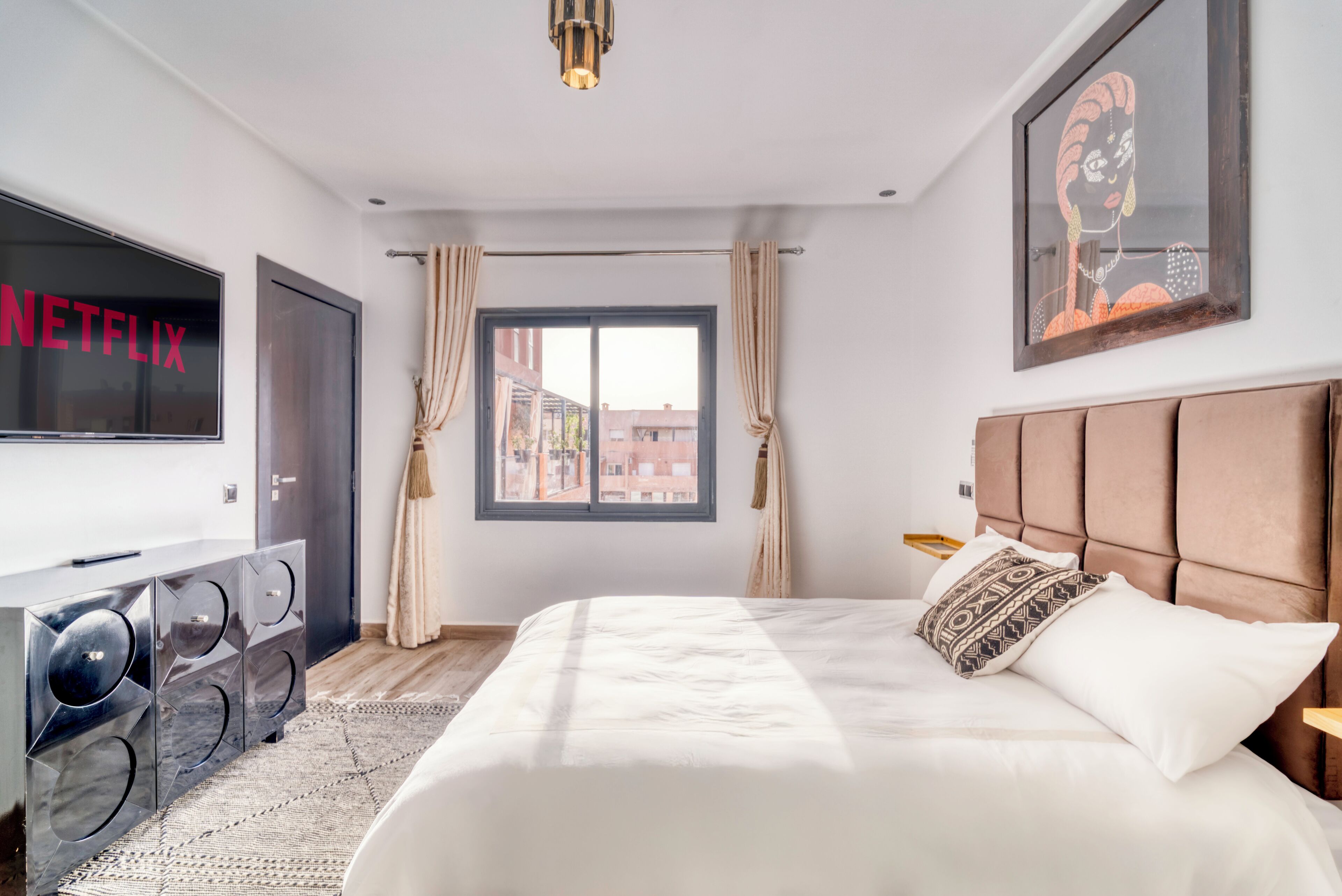 Una habitación de hotel moderna con una cama grande, un televisor de pantalla plana, una ventana con cortinas y vistas a edificios.