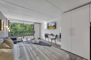 A modern bedroom with a large bed, a desk, and a chair, a TV, and a wardrobe. - Cozy Family Escape Near Disney + Parking | Orl (Kissimmee)