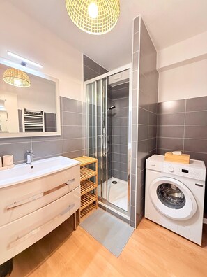 A modern bathroom with a glass-enclosed shower, a built-in washing machine, and a vanity with a mirror.
