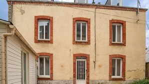Edifici de dues plantes amb façana de maó, nombroses finestres i una petita zona exterior amb una taula i cadires.