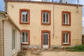 A two-story building with a brick facade, multiple windows, and a small outdoor seating area with a table and chairs. - L'Élégante - Petfriendly - Proche gare (Laval)