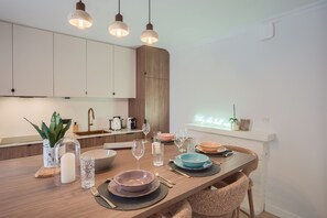 A modern kitchen with a wooden dining table set for four, equipped with a sink, kettle, and various kitchen appliances. - L'Élégante - Petfriendly - Proche gare (Laval)