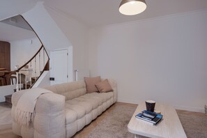 Ein modernes Wohnzimmer mit einem beigefarbenen Sofa, einem Couchtisch mit Büchern, einer Treppe und einer weißen Decke.