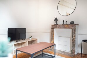 A modern living room with a television, a small table, a fireplace, and a mirror on the wall. - L'Espine - Hyper centre - Tramway (Angers)