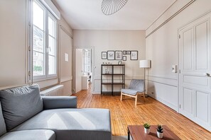 A modern living room with a grey sofa, wooden flooring, a bookshelf, and a lamp. - L'Espine - Hyper centre - Tramway (Angers)