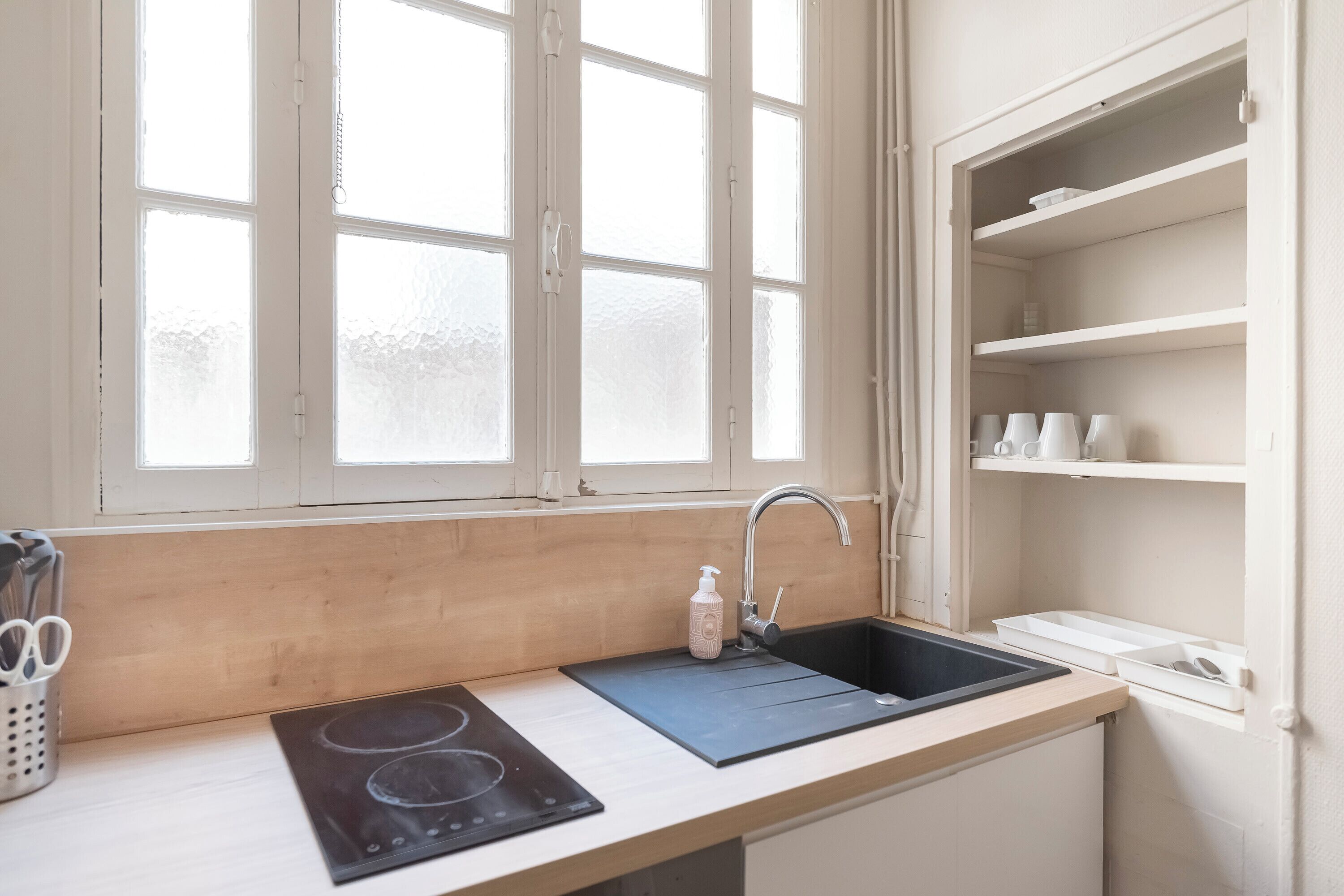 A kitchen with a window, a sink, a stove, and shelves.