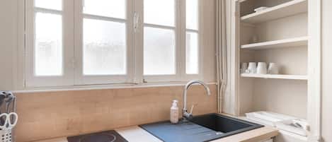A kitchen with a window, a sink, a stove, and shelves.