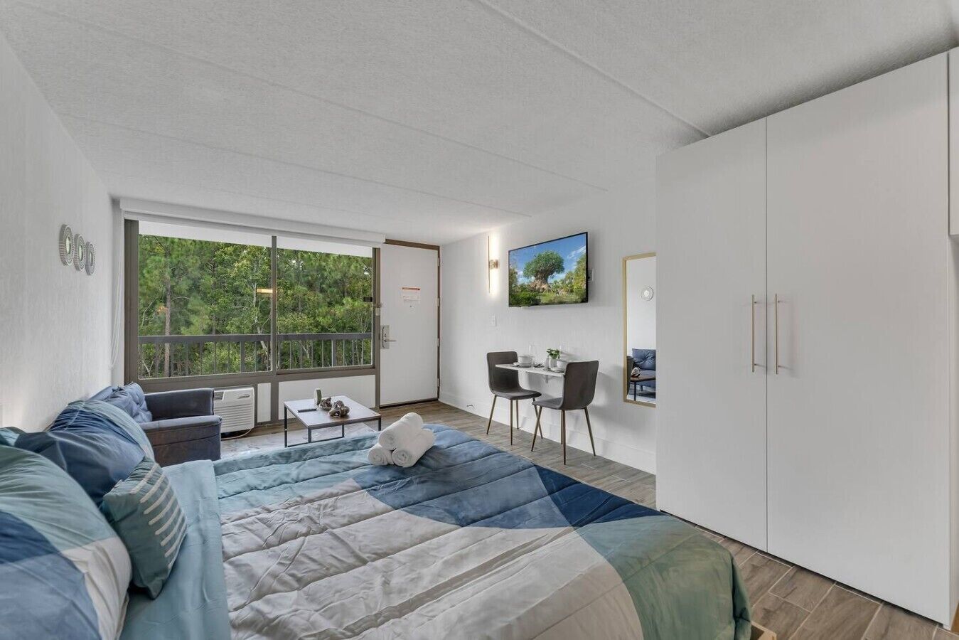 Een moderne slaapkamer met een groot bed, een balkon met uitzicht op bomen, een zithoek en een kledingkast.