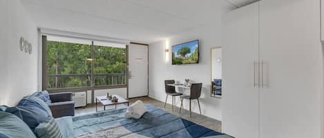 Een moderne slaapkamer met een groot bed, een balkon met uitzicht op bomen, een zithoek en een kledingkast.