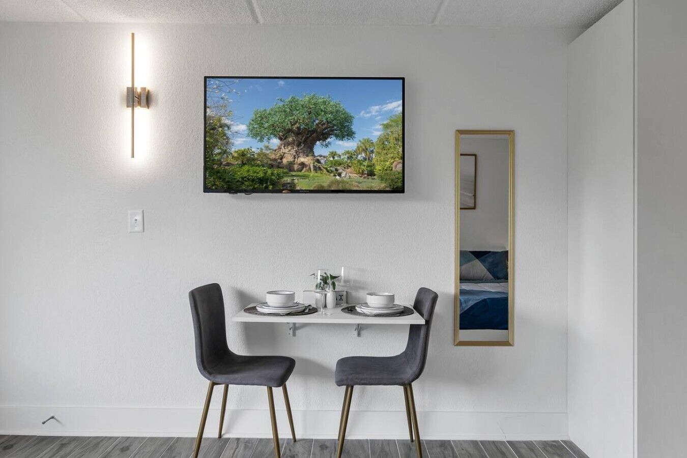 A modern dining area with a table set for two, a wall-mounted TV, and a framed picture above the table.
