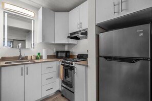 Una cocina moderna con armarios blancos, un refrigerador de acero inoxidable, un microondas, una estufa y un lavabo.