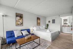 A modern, well-lit room with a blue sofa, a wooden coffee table, a large bed with white bedding, and a small bedside table. - Top Disney Location w Pool & Free Parking | Orl (Kissimmee)