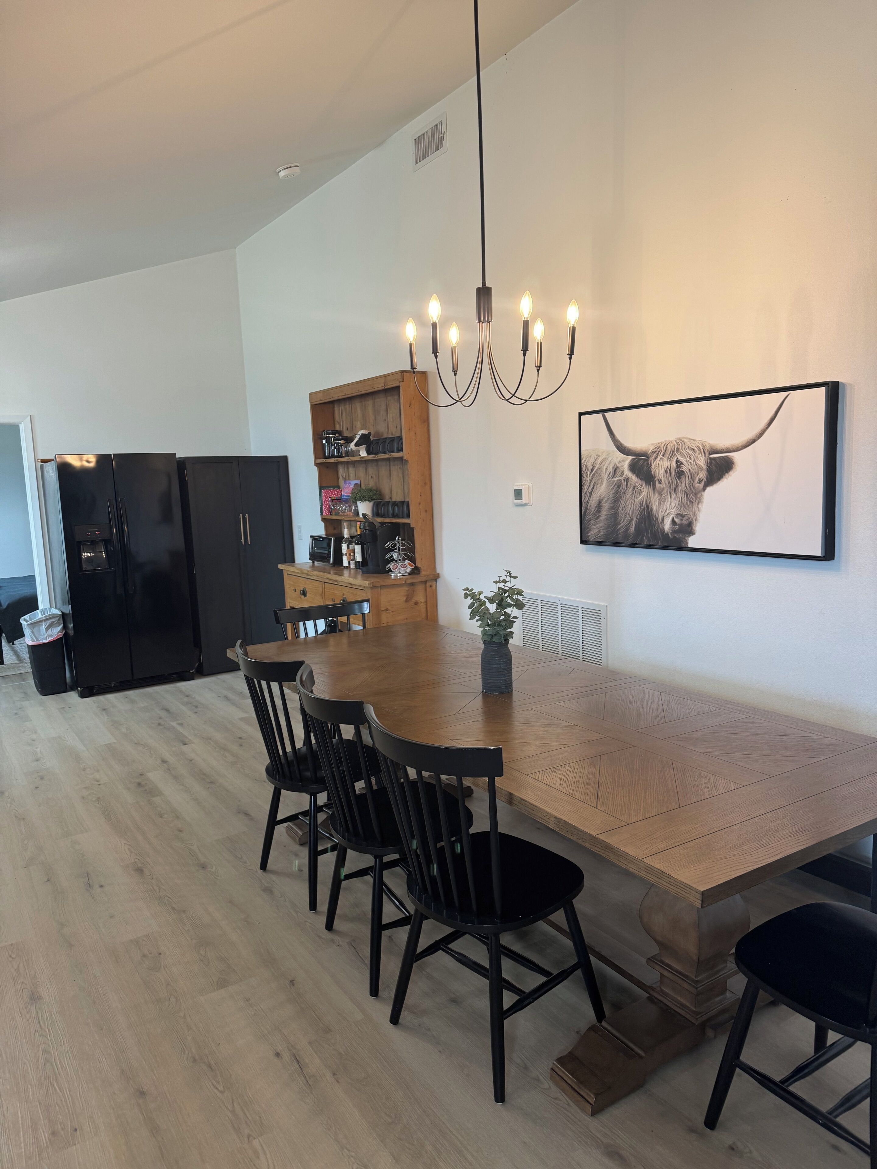 A modern kitchen with black appliances, a wooden dining table, and a chandelier.