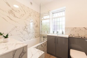 Ein modernes Badezimmer mit Waschtisch aus Marmor, einer Badewanne und einer Toilette.