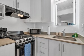 A modern kitchen with a gas stove, microwave, and stainless steel sink. - Resort Condo 7 Min to Disney | Free Parking | Orl (Kissimmee)