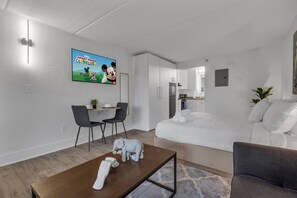 Une chambre d’hôtel moderne comprenant un coin repas, un lit et un téléviseur diffusant l’émission « La maison de Mickey ».