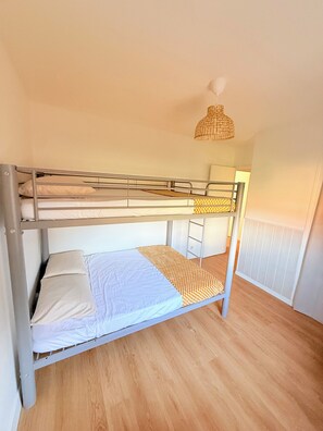 Ein Stockbett mit weißer Matratze und einem gemusterten Überwurf, eine Korblampe und eine Heizung in einem Zimmer mit Holzboden.