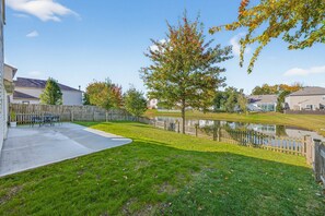 A residential backyard with a paved patio, a small pond, and a wooden fence. - Roadmap Lodging: Geist Waterfront 4BR, Fishers (Fishers)