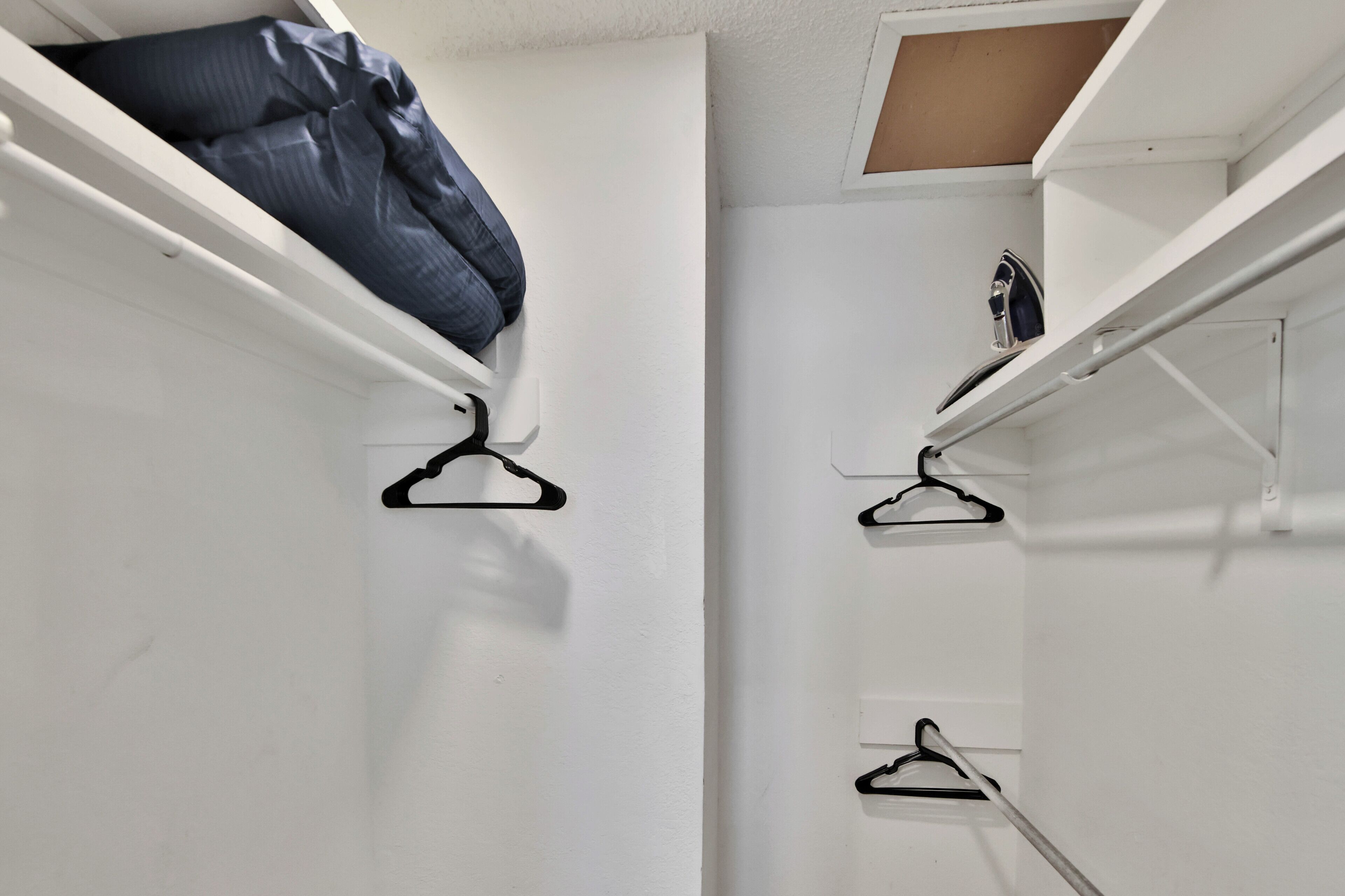 A white closet with three black hangers and a folded blue garment on the top shelf.