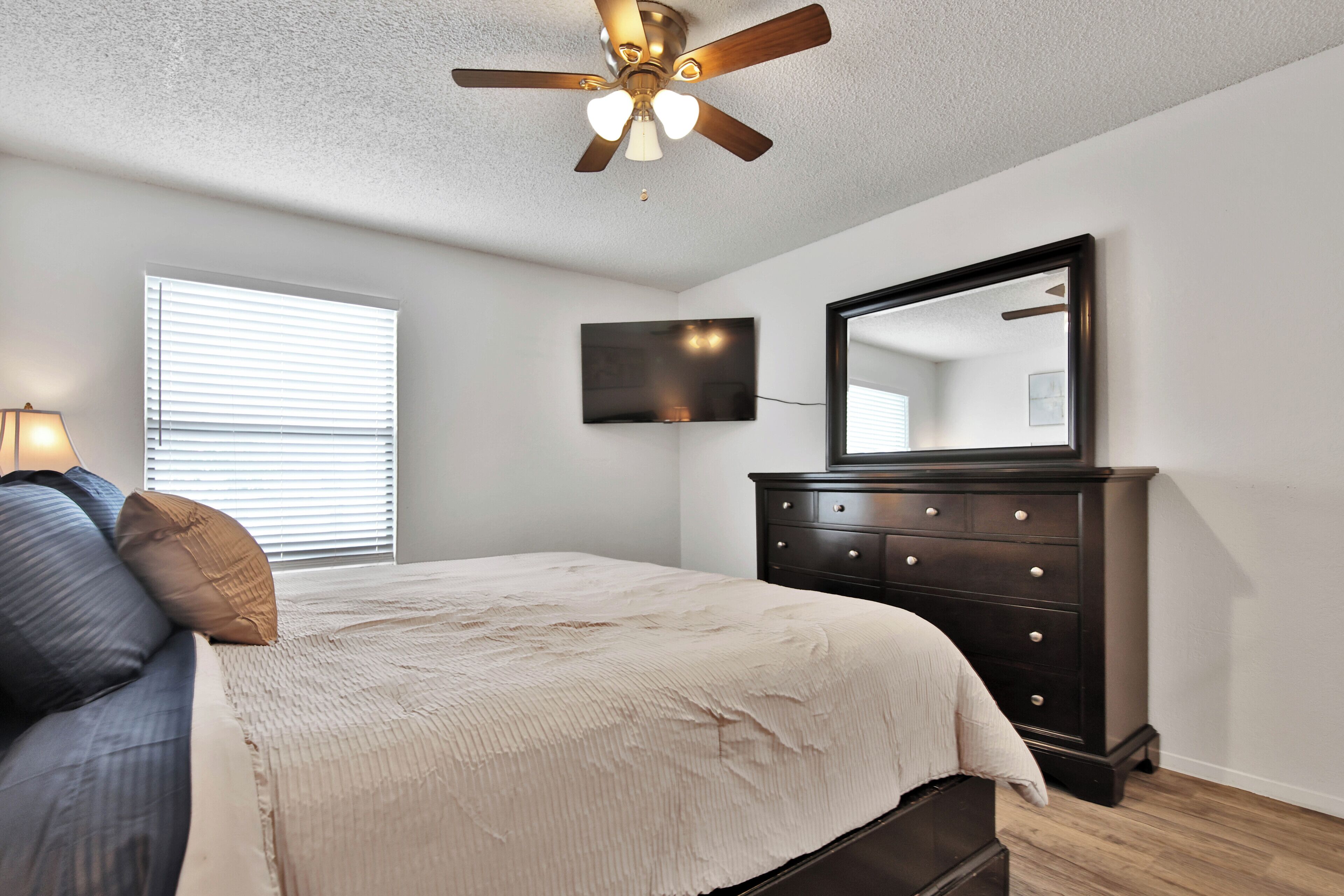 A bedroom with a bed, a dresser, a ceiling fan, a TV, and a window with blinds.