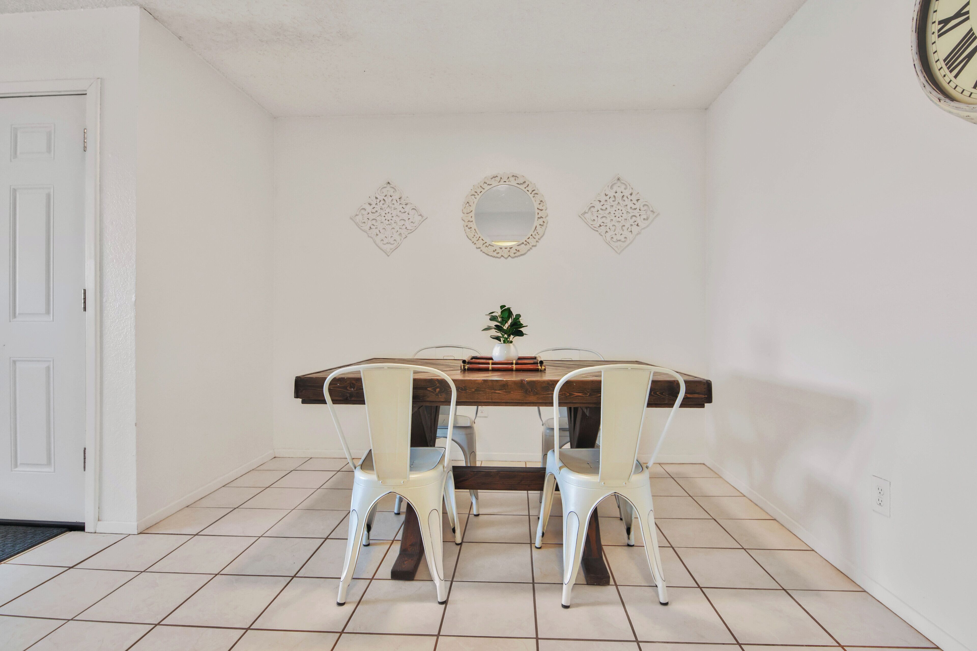 A dining area with a wooden table, white chairs, and decorative wall mirrors.