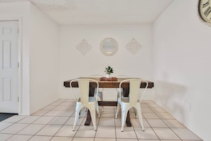 Un área de comedor con una mesa de madera, sillas blancas y espejos decorativos en la pared.