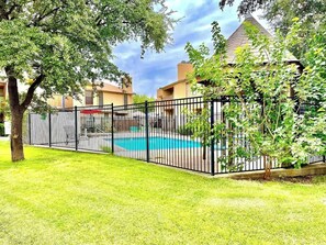 Une piscine clôturée, dont l’eau est d’un bleu limpide, entourée d’une pelouse et d’arbres.